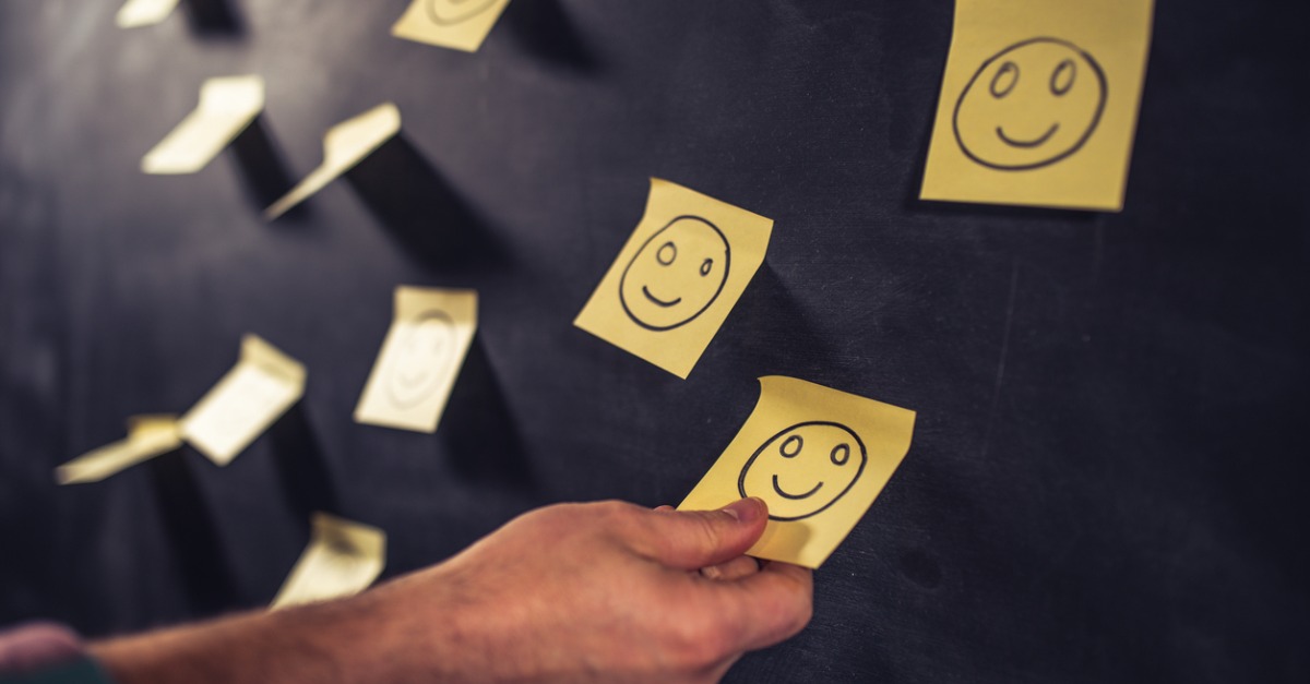 Individual placing smiley face sticky note on the wall